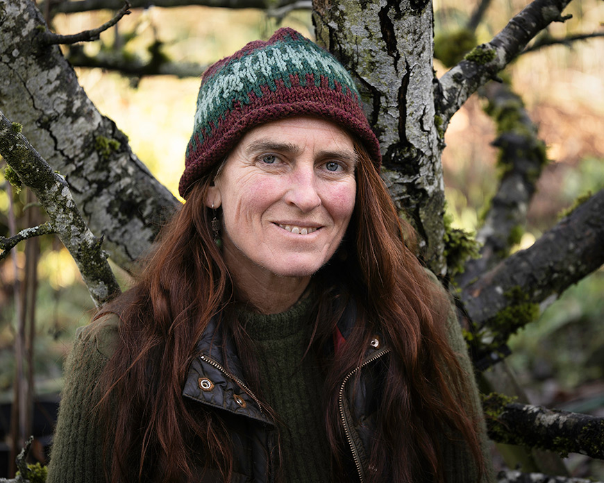 A woman in a knit hat sitting outside in front of a tree.